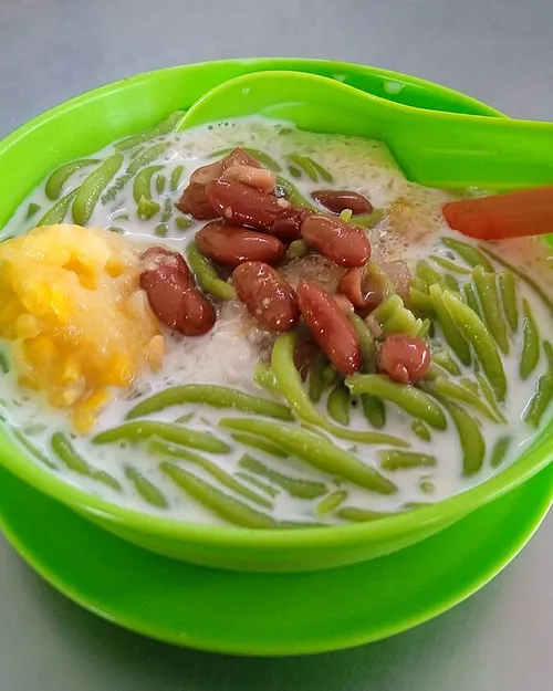 Cendol in a bowl with shaved ice, green rice noodles, coconut milk, and dark palm sugar syrup