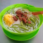 Cendol in a bowl with shaved ice, green rice noodles, coconut milk, and dark palm sugar syrup