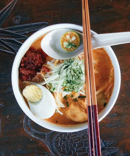 Curry laksa in a bowl with coconut broth, rice noodles, prawns, and tofu puffs
