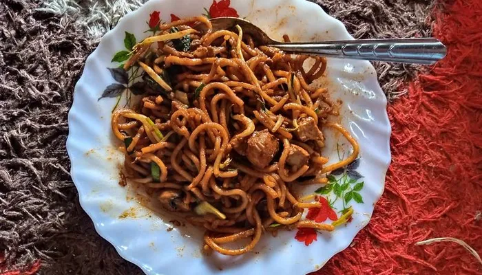 Mee goreng mamak in a wok-fried heap of yellow noodles, egg, and vegetables with a dark sauce