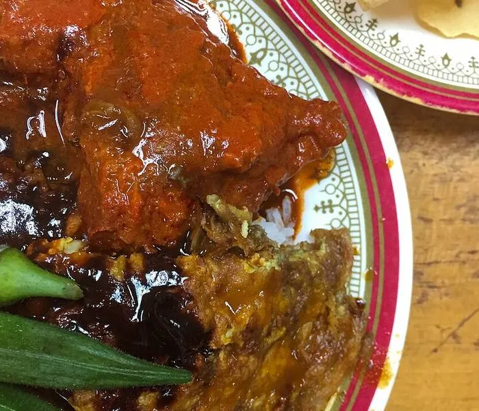 Nasi kandar plate with white rice and several curry sauces poured over, with a piece of fried chicken