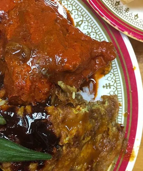 Nasi kandar plate with white rice and several curry sauces poured over, with a piece of fried chicken