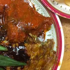 Nasi kandar plate with white rice and several curry sauces poured over, with a piece of fried chicken
