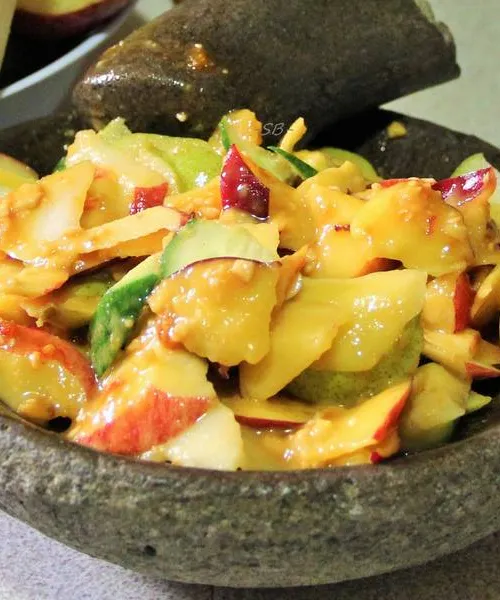Rojak salad with sliced fruits, cucumber, and tofu in a dark thick sauce topped with crushed peanuts