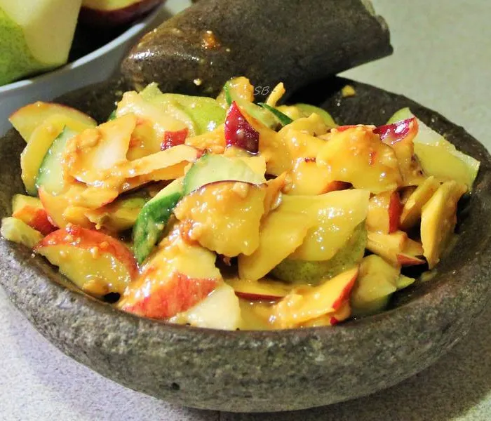 Rojak salad with sliced fruits, cucumber, and tofu in a dark thick sauce topped with crushed peanuts