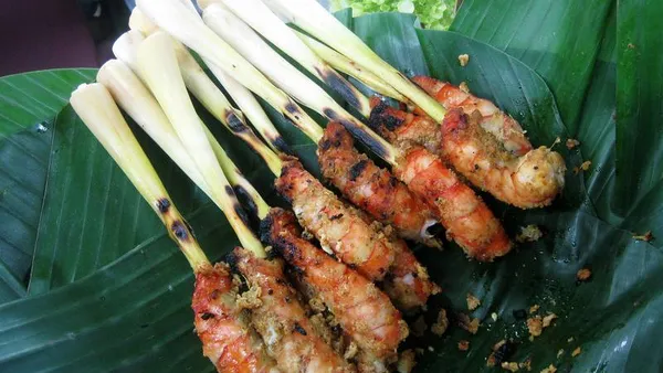 Chicken satay skewers on a charcoal grill, with peanut sauce and cucumber
