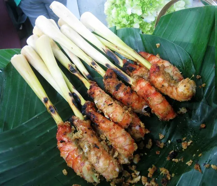 Chicken satay skewers on a charcoal grill, with peanut sauce and cucumber