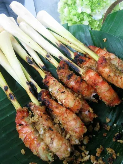 Chicken satay skewers on a charcoal grill, with peanut sauce and cucumber