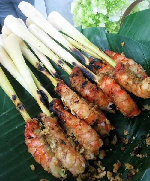 Chicken satay skewers on a charcoal grill, with peanut sauce and cucumber