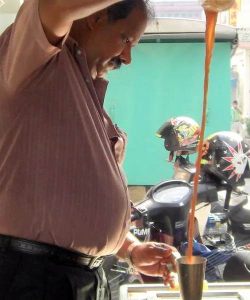 Teh tarik being poured from height between two metal cups, creating a thick froth