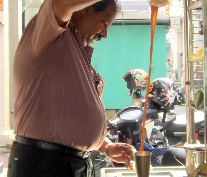 Teh tarik being poured from height between two metal cups, creating a thick froth